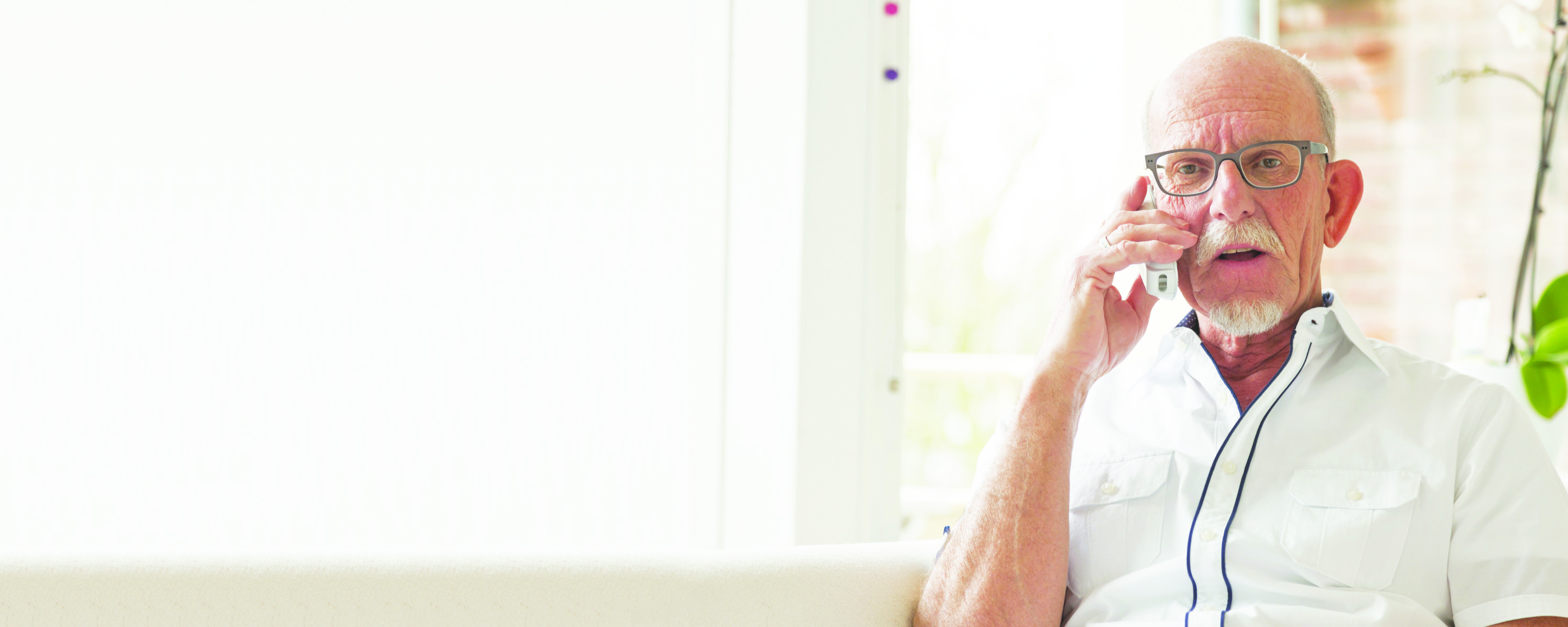 Senior man calling with portable phone in living room.