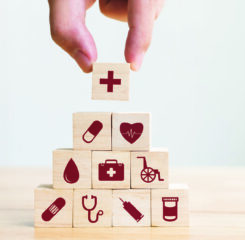 A hand stacking blocks with medical icons to emphasize the importance of having a strong healthcare strategy.