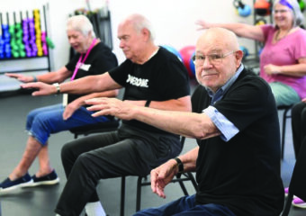 Man in a class with other seniors at a senior center, looking at the camera and smiling, enjoying the camaraderie and activities.