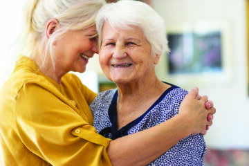 A caregiver hugging an elderly woman, both smiling.