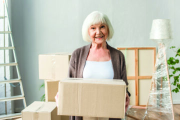 Older woman holding moving boxes during a home transition representing downsizing and senior relocation