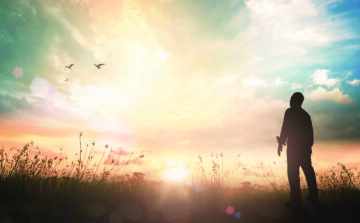 Silhouette of a man standing in a field at sunrise, gazing toward the light
