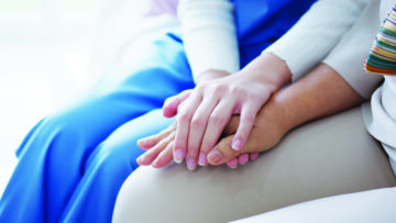 Close-up of a caregiver’s hand gently holding a patient’s hand