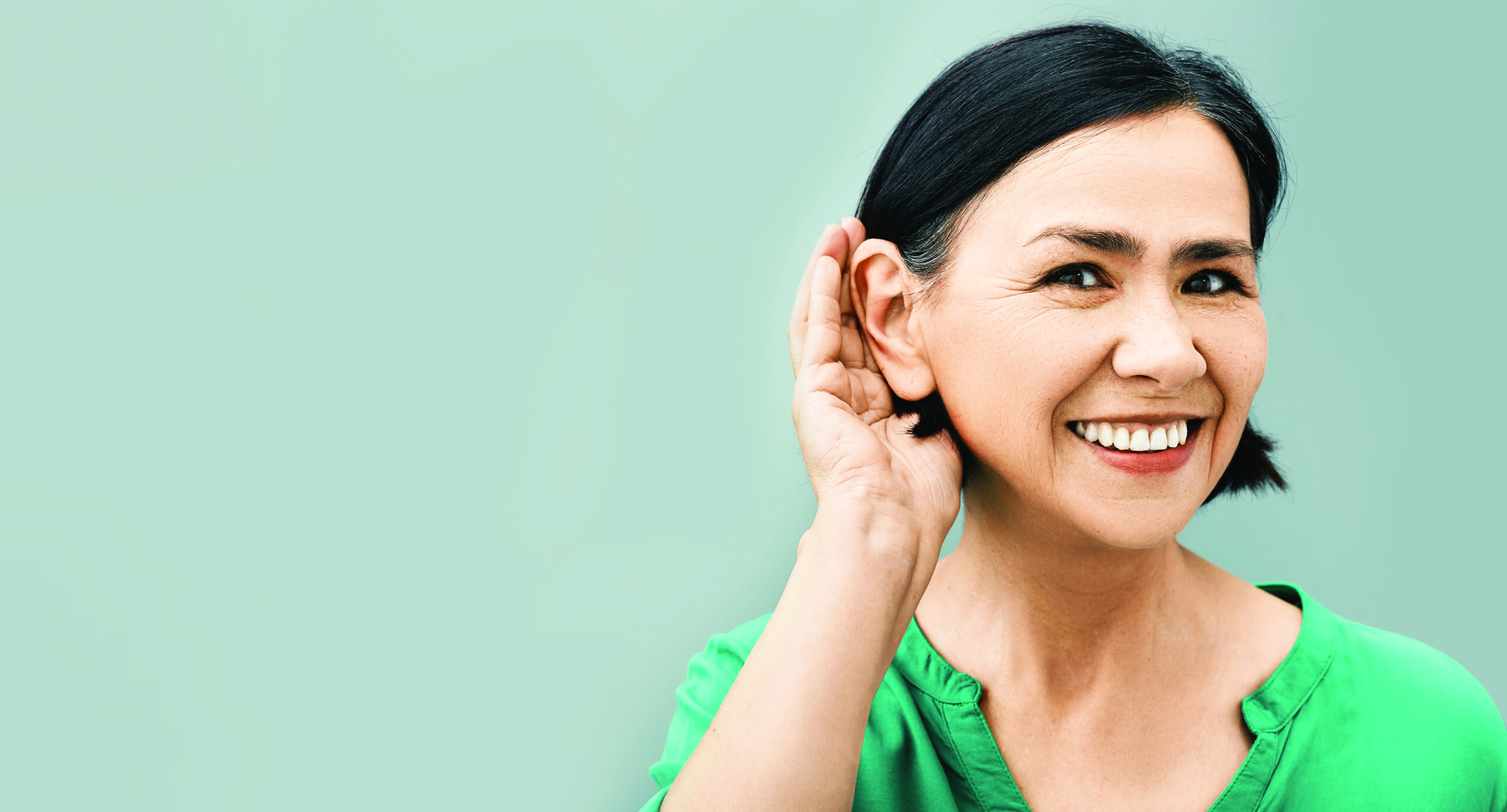 Smiling middle-aged woman holding her hand to her ear as if listening closely.