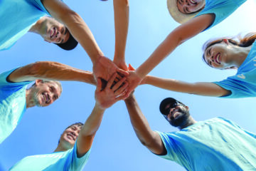 Diverse group of volunteers stacking hands together outdoors Title: Volunteering and Community Connection