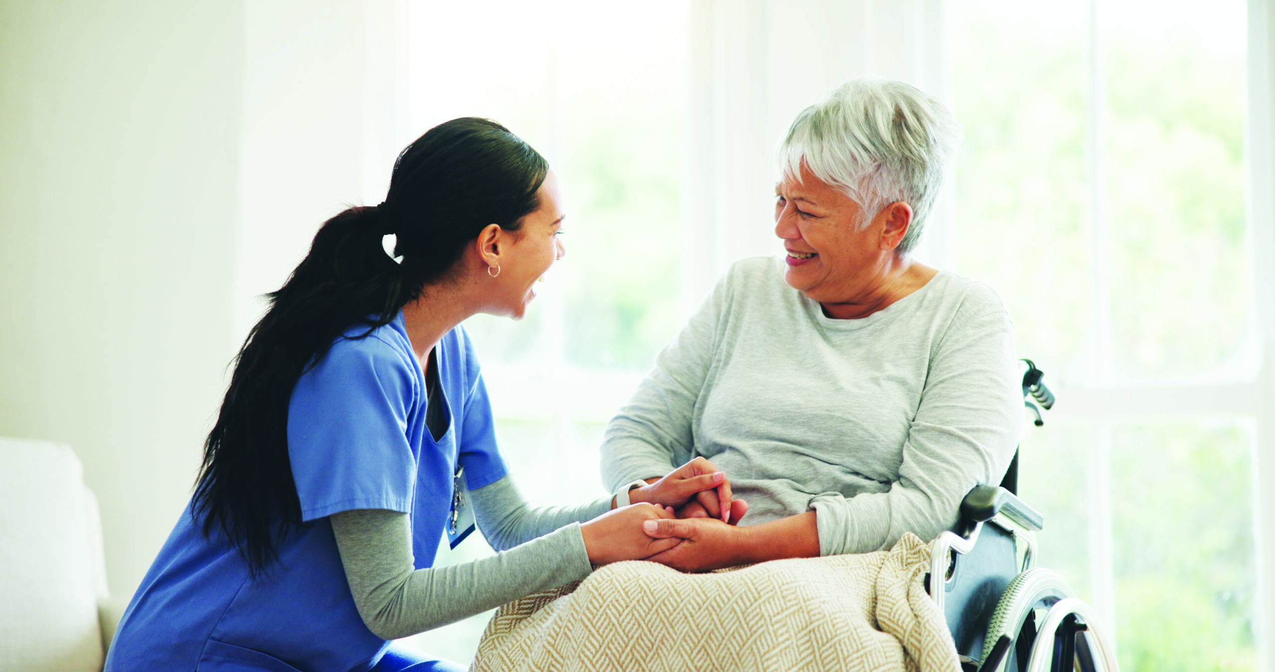 Caregiver holding hands and talking with an older woman in a wheelchair