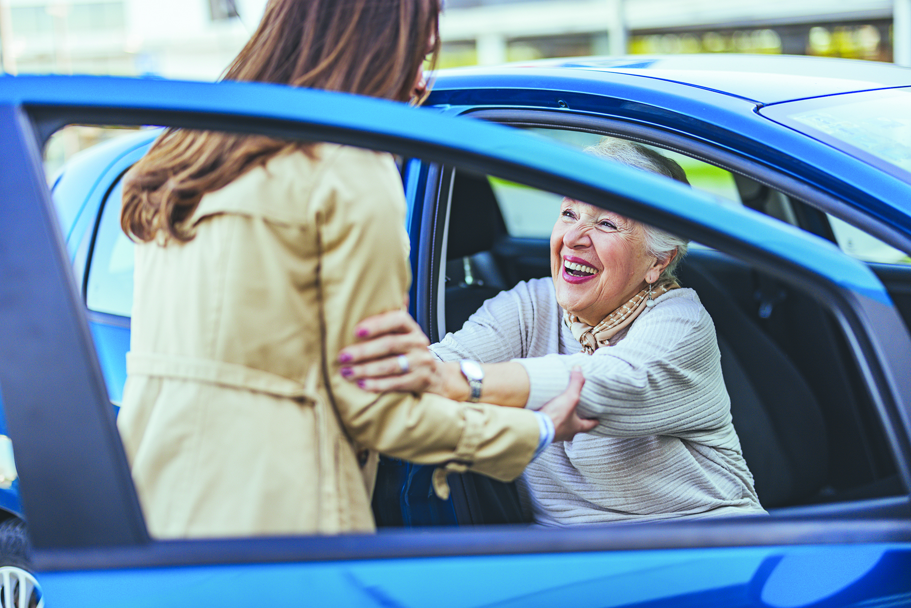 Elderly woman smiles as she receives assistance exiting a car