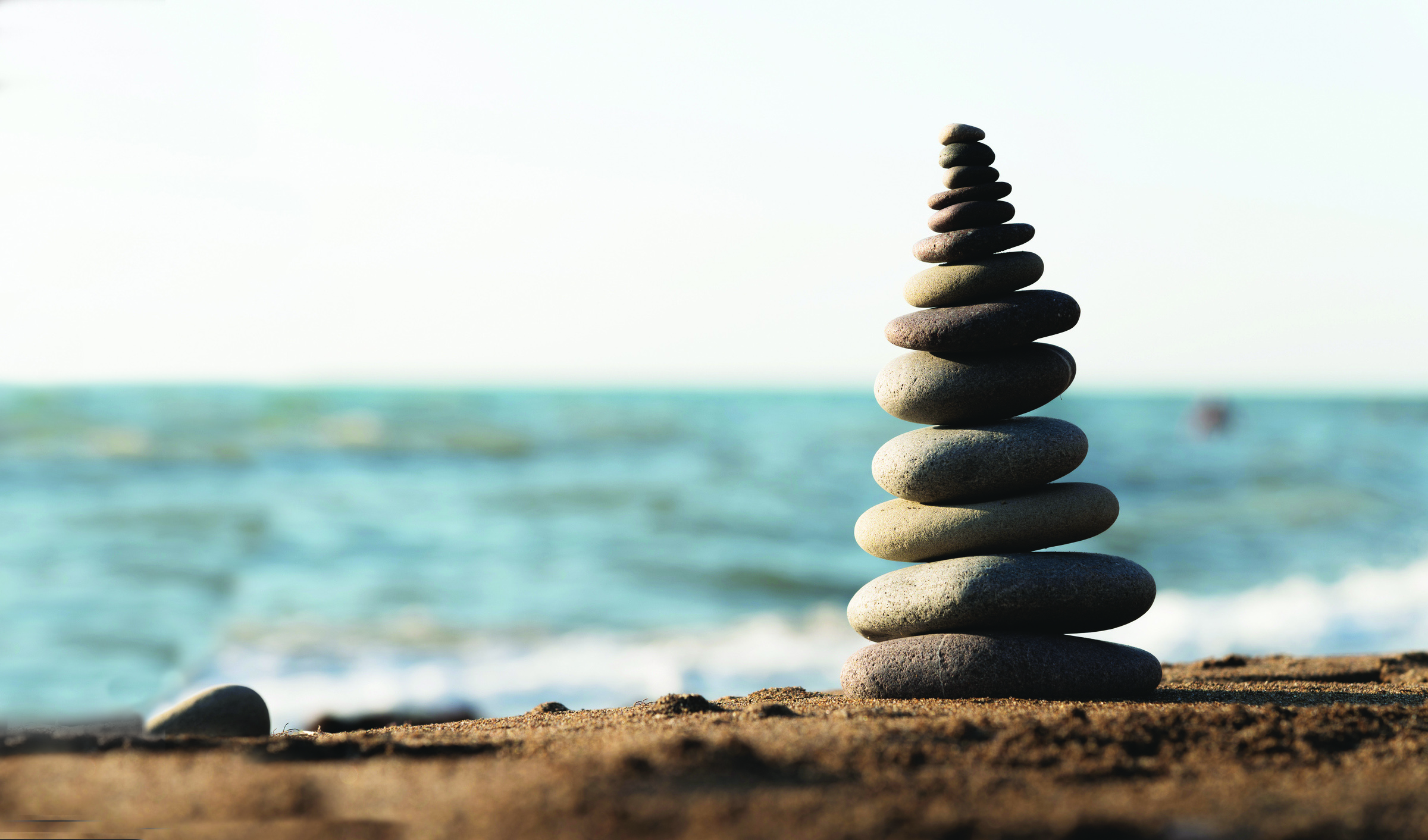 Stacked stones of remembrance on a sandy beach with ocean waves, symbolizing God’s miracles and the R.O.C.K. acronym from Joshua 4