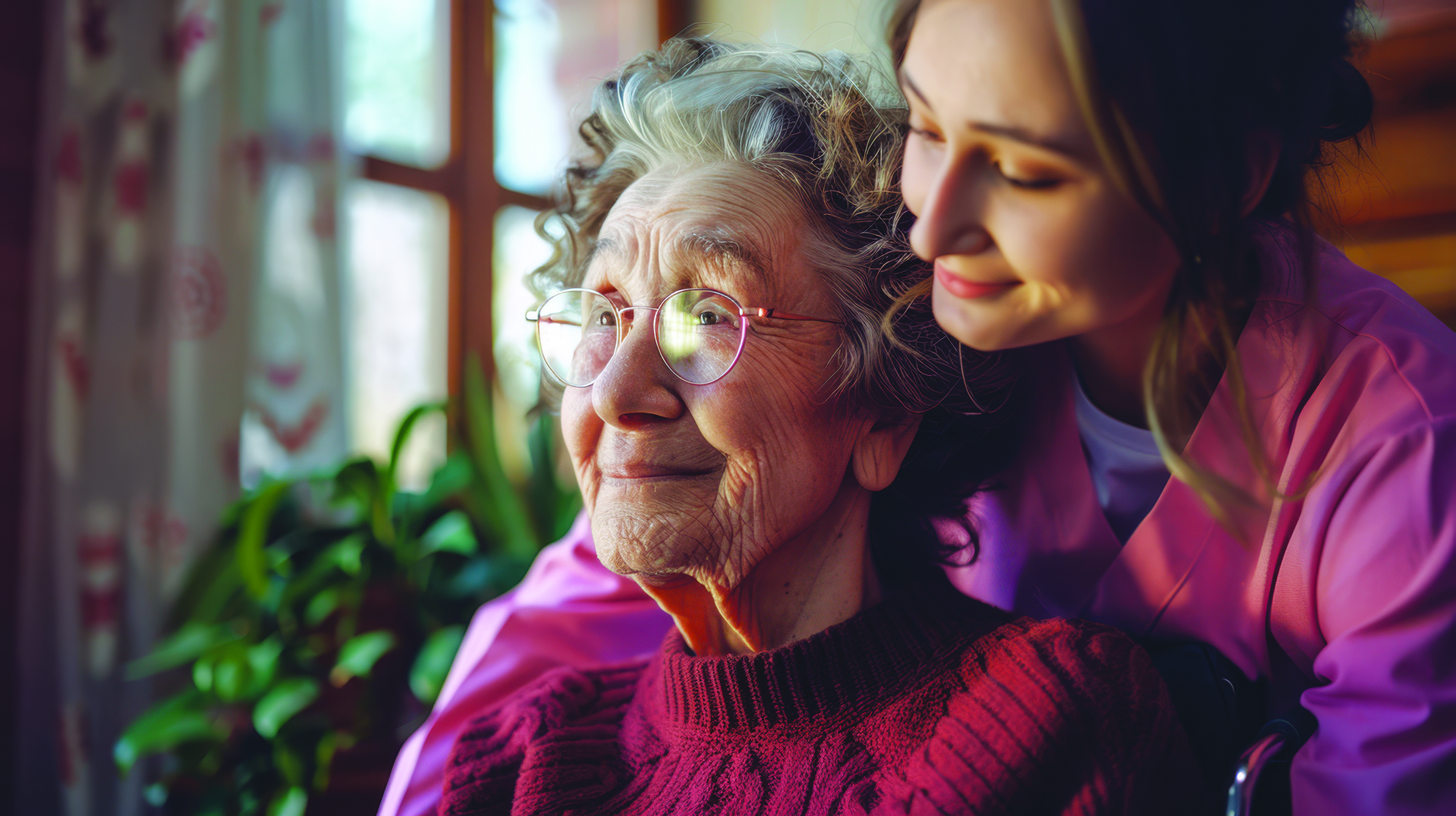 Elderly woman in red sweater smiling as a young caregiver leans close with affection.